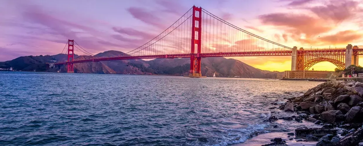 El puente Golden Gate al atardecer con un cielo multicolor y la Bahía de 贝博体彩app en primer plano.